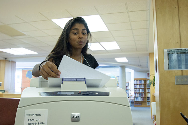 Finding an assignment for class, senior Isabel Marshall-Kramer picks up her paper at the librarys printer. The library printer offers free printing to all students. Conscious of funding, teachers have been asking students to print from home, if possible.