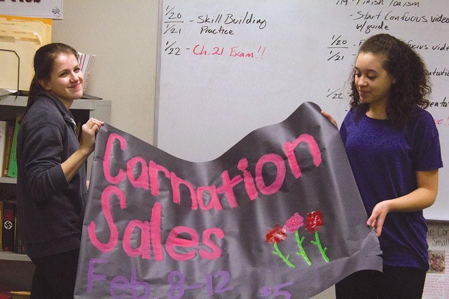 Prepping for their Valentines Day carnation sales, junior Katie Lane and freshman Tylee Harrell display their recently finished banner.