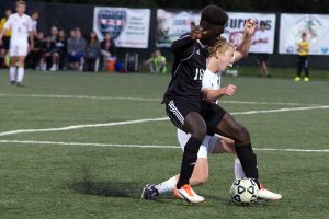 LHS player Ebrahim Diagne battles senior Owen Kapfer for possession of the ball. The soccer field was decorated with posters signed by students displaying "#KapferStrong".