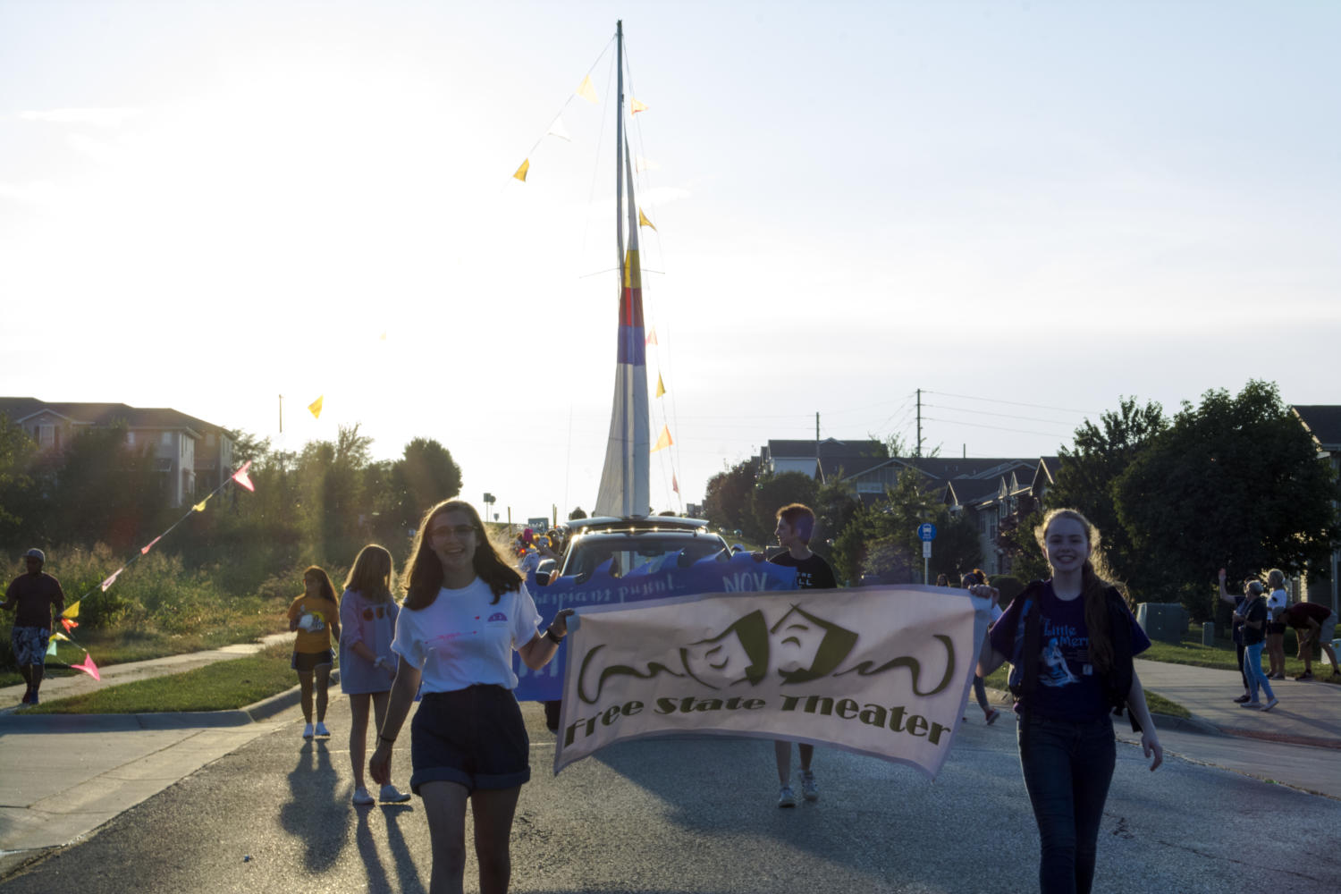 Junior Sophie Johnson and freshmen Emily Bial carry the Free State Theater banner in the homecoming parade. A float for the musical Anything Goes followed behind them.