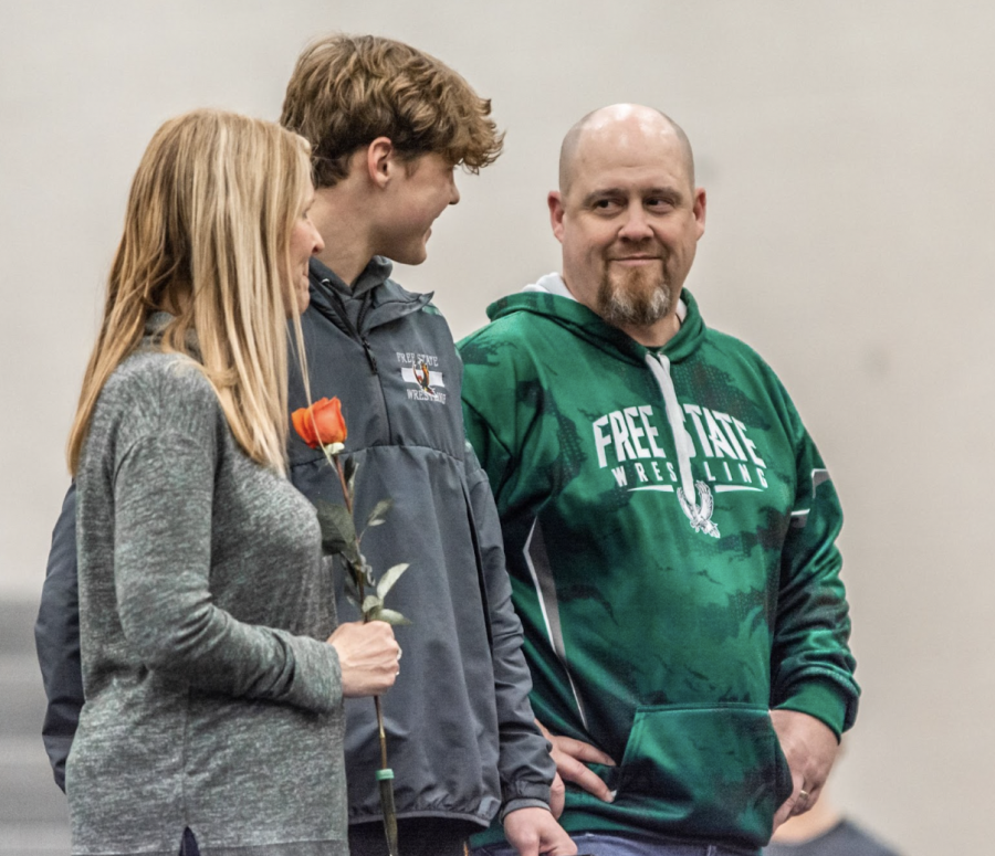 Head Varsity boys wrestling coach, Randy Streeter smiles at his son, Eric Streeter, as the commentator reads about his accomplishments on senior night. 