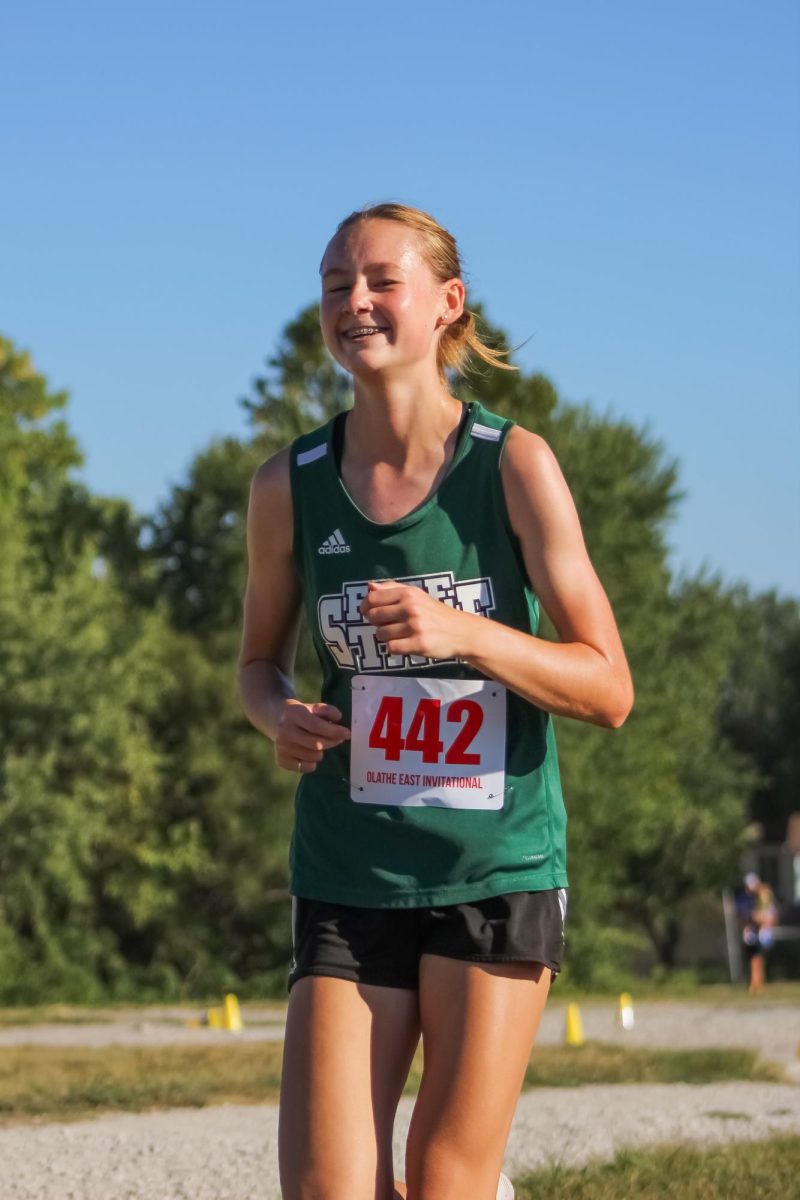 Smiling, sophomore Harper Graham strides through her race. This is her first year on the cross country team after running distance and throwing in track and field last spring. 