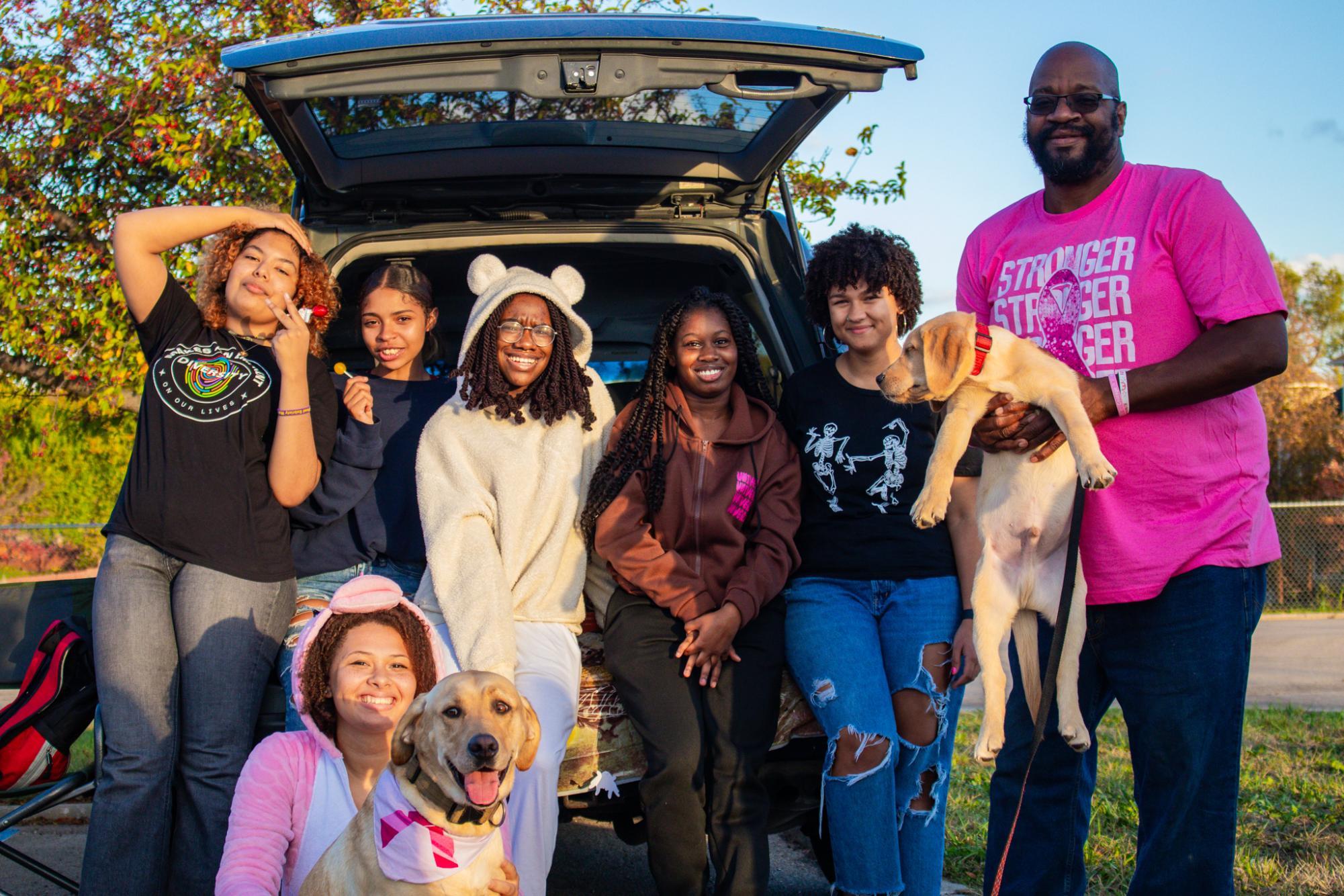 Security guard Demetrius Kemp poses with Free state therapy dog Wayne and new addition Marlo along with students at the Trunk-or-Treat.