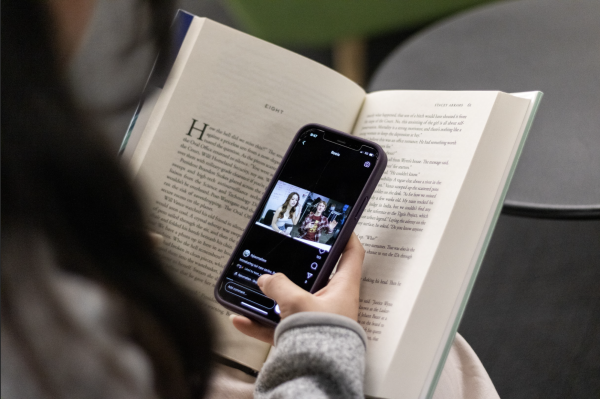  A student scrolls through Instagram while hiding their phone in a book. Many students employ similar tactics to get out of reading. 
