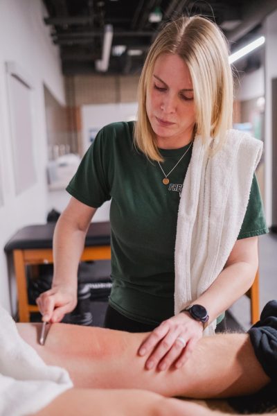 Working with a student, athletic trainer Kaarin Haig scrapes a students leg. In the spring season many athletes come into this physical training space in order to get help with their injuries.