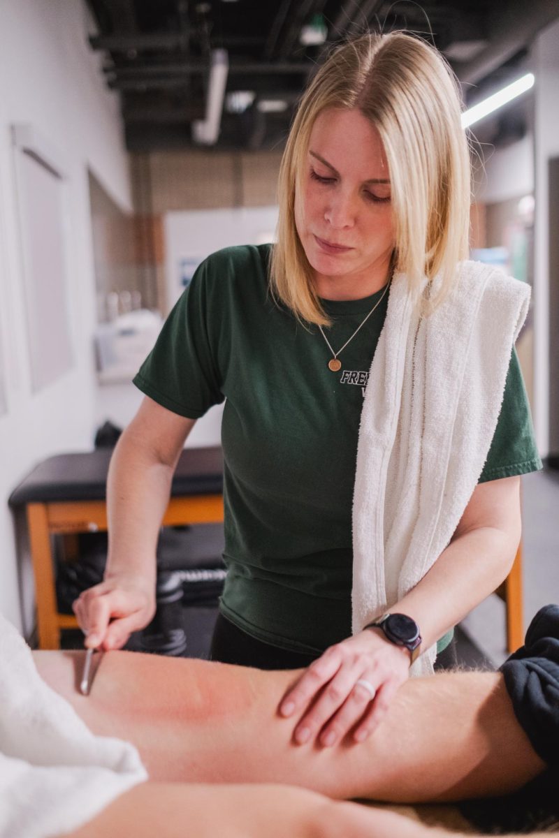 Working with a student, athletic trainer Kaarin Haig scrapes a students leg. In the spring season many athletes come into this physical training space in order to get help with their injuries.