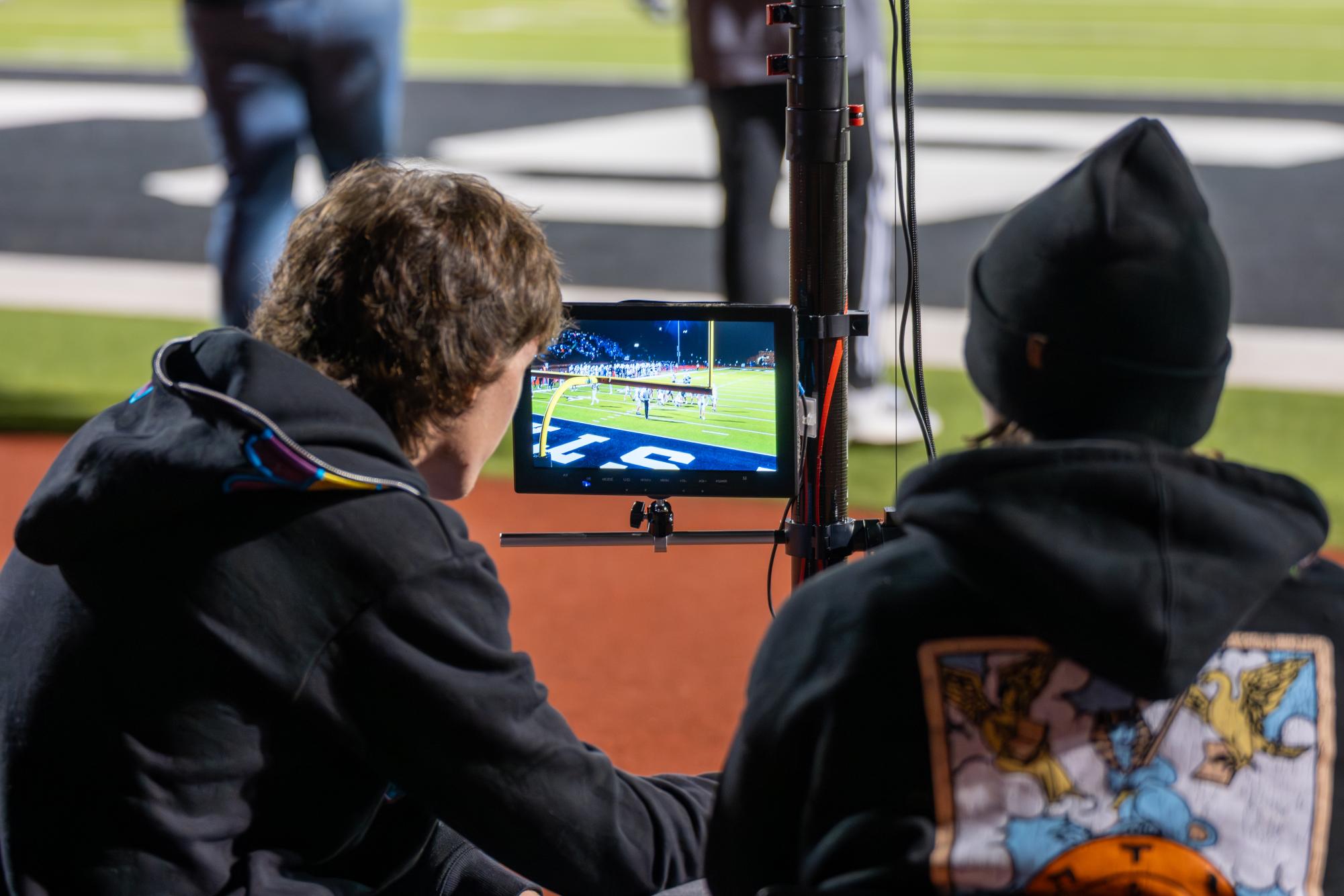 Behind a camera, senior Liam Smith and junior Liam Butler film the football team during a game.